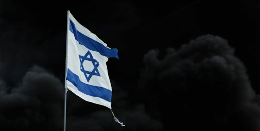 Israeli flag seen in front of burned barricade in settlement of Katif in Gush Katif bloc of Jewish settlements. An Israeli flag is seen in front of a burned barricade in the settlement of Katif in the Gush Katif bloc of Jewish settlements, in the southern Gaza Strip, August 21, 2005. Israeli forces marched into a cluster of Jewish enclaves in Gaza on Sunday to remove tearful settlers and complete the evacuation of the biggest settlement bloc in the occupied territory. REUTERS/Goran Tomasevic - RTRL6W4